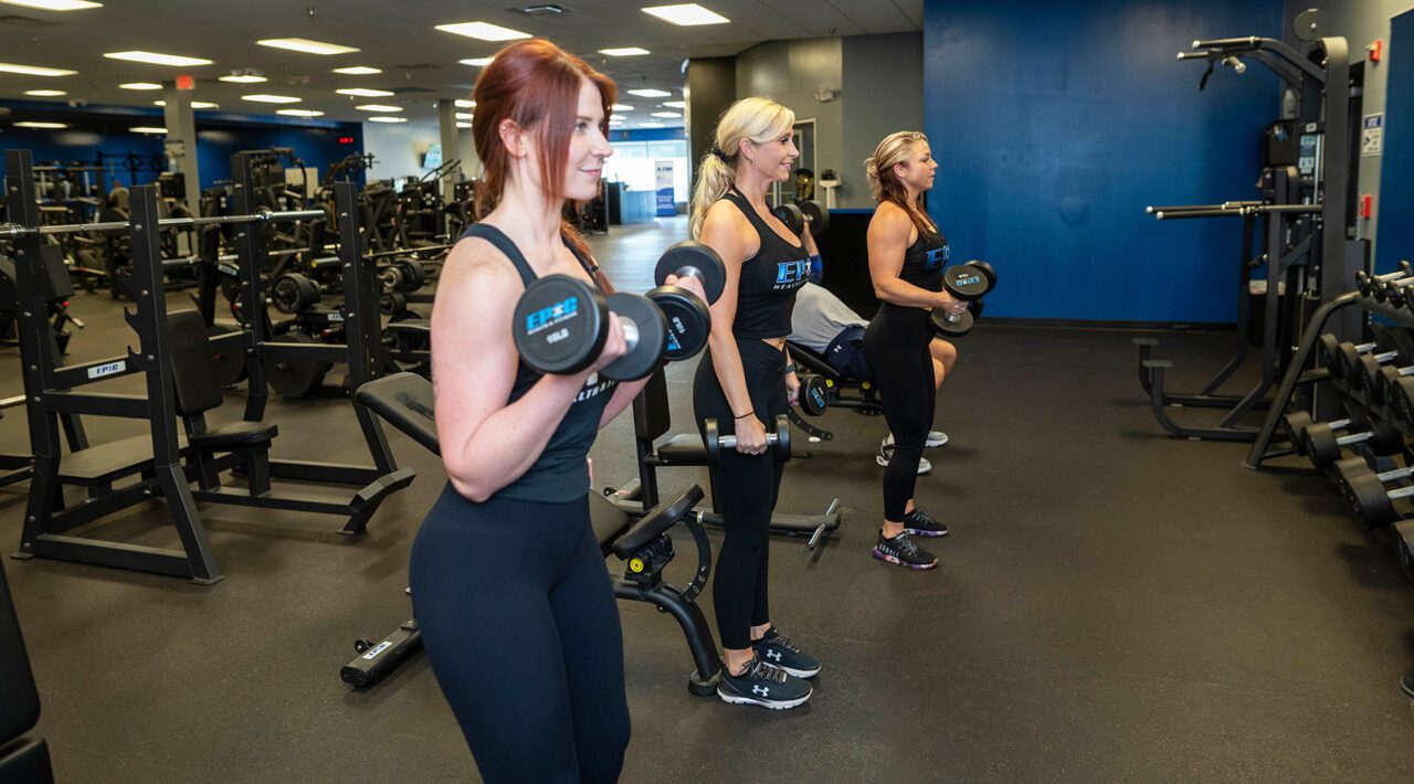 Women lifting dumbbells at Epic Fitness gym in New Hampshire, focused on strength training, goal-oriented fitness routines, muscle toning, and personalized health transformations.